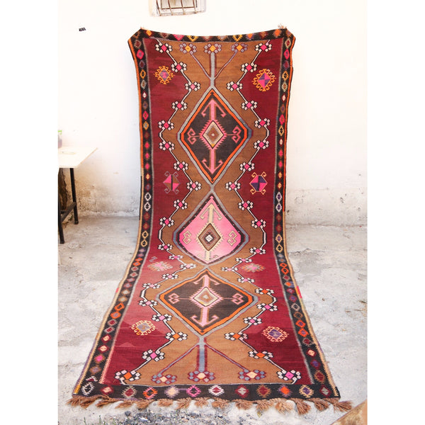This large vintage Kars Turkish kilim has a beautiful field of a light burgundy with camel, pink, and yellow accents. 
